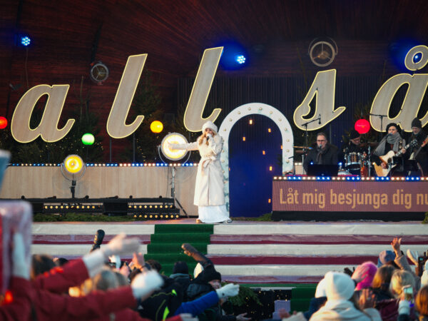 Pernilla Wahlgren står på scen i vita vinterkläder och sjunger i mikrofon