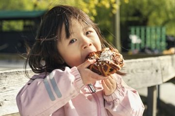 En liten flicka som äter en bulle medan hon sitter på en bänk.